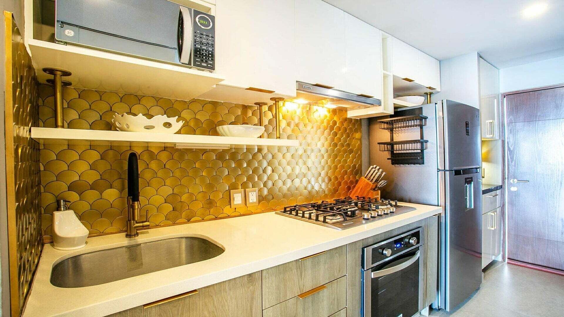 Une cuisine moderne dotée d’une cuisinière à gaz, d’appareils électroménagers en acier inoxydable et d’un revêtement mural original en forme de nid d’abeilles.