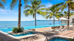 A pool area with lounge chairs, palm trees, and a view of the ocean. - Wake Up to Stunning Beach & Harbor Views (Puerto Vallarta)