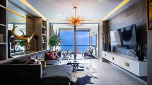 Ett modernt vardagsrum med en soffa, ett soffbord och dekorativa föremål. Det finns ett stort fönster med utsikt över havet.