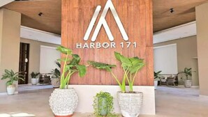 En träskylt med texten ”HARBOR 171” och en logotyp, omgiven av stora krukväxter.
