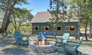 A lodge with a fire pit, outdoor seating, and a view of the surrounding forest.