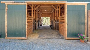 A covered stable with open stalls, a gravel path, and a potted plant. - Barndo Hideaway at Hy Sun Ranch (Auburn)