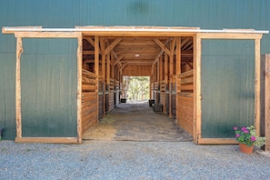 A covered stable with open stalls, a gravel path, and a potted plant.