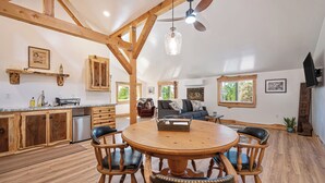 A spacious kitchen with wooden beams, a dining area with a round table and chairs, and a living room with a sofa and a television. - Barndo Hideaway at Hy Sun Ranch (Auburn)