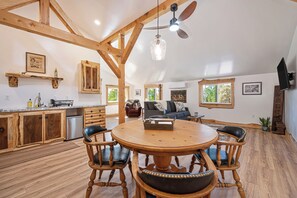 A spacious kitchen with wooden beams, a dining area with a round table and chairs, and a living room with a sofa and a television.