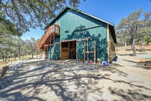 A rustic barn-style building with a wooden staircase, large windows, and a gravel driveway.