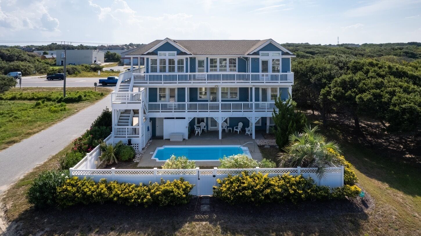 A two-story house with a swimming pool, surrounded by a white fence and greenery.