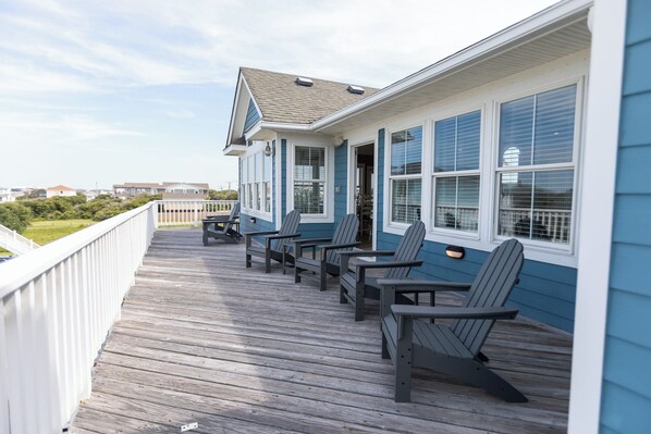 A wooden deck with Adirondack chairs, a white railing, and a building with blue siding and white trim. - Oceanside, Pool, Walk to Beach! Pet Friendly! (Kitty Hawk)
