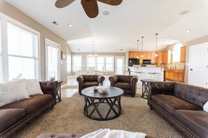 A spacious living room with leather sofas, a round coffee table, and a kitchen in the background. - Oceanside, Pool, Walk to Beach! Pet Friendly! (Kitty Hawk)