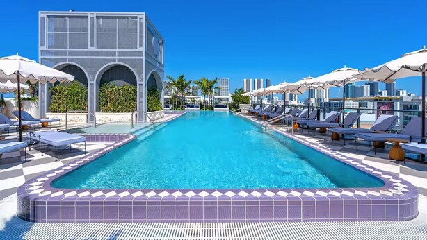 A swimming pool with lounge chairs and umbrellas, a modern building with arched windows, and a clear blue sky. - NoMad Residences Wynwood FIFA Fan Stay (Miami)