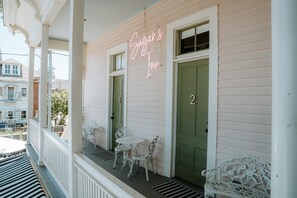 En byggnad med en neonskylt som visar texten ”Sugar’s Inn”, en grön dörr och vita utemöbler på verandan.