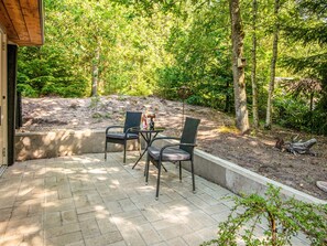 Eine Terrassengruppe im Freien mit zwei Stühlen und einem Tisch, umgeben von einer Betonkante und einem bewaldeten Bereich.