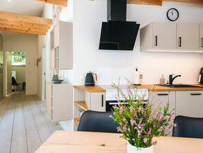 Eine moderne Küche mit Herd, Spüle und Schränken, einer Uhr an der Wand und einer Holzbalkendecke.