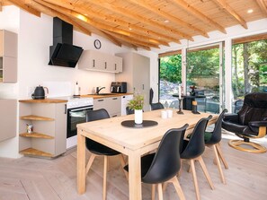 A modern kitchen with a wooden ceiling, a dining area with a table and chairs, and a view of the outdoors through large windows. - 5 Star Holiday Home in Ans By (Ans)