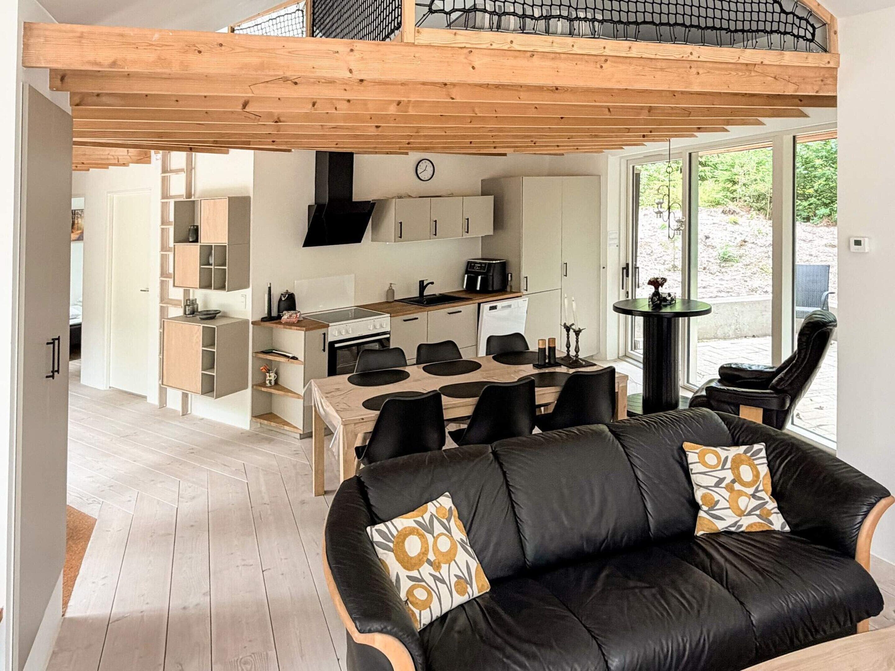 Une cuisine moderne avec un coin repas, un canapé en cuir noir agrémenté de coussins à motifs et un plafond en bois.