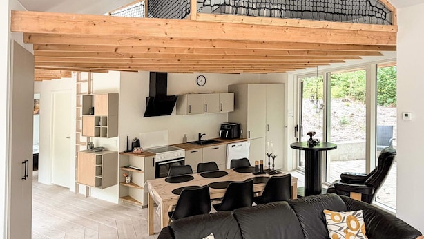 Ett modernt kök med en matplats, en svart lädersoffa med mönstrade kuddar och ett träpanelat tak.