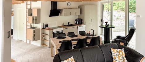 A modern kitchen with a dining area, a black leather sofa with patterned cushions, and a wooden ceiling.