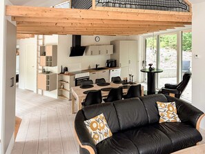 A modern kitchen with a dining area, a black leather sofa with patterned cushions, and a wooden ceiling. - 5 Star Holiday Home in Ans By (Ans)