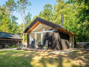 Una cabaña moderna con un amplio acceso por puerta de vidrio, una terraza con mobiliario exterior y una chimenea.