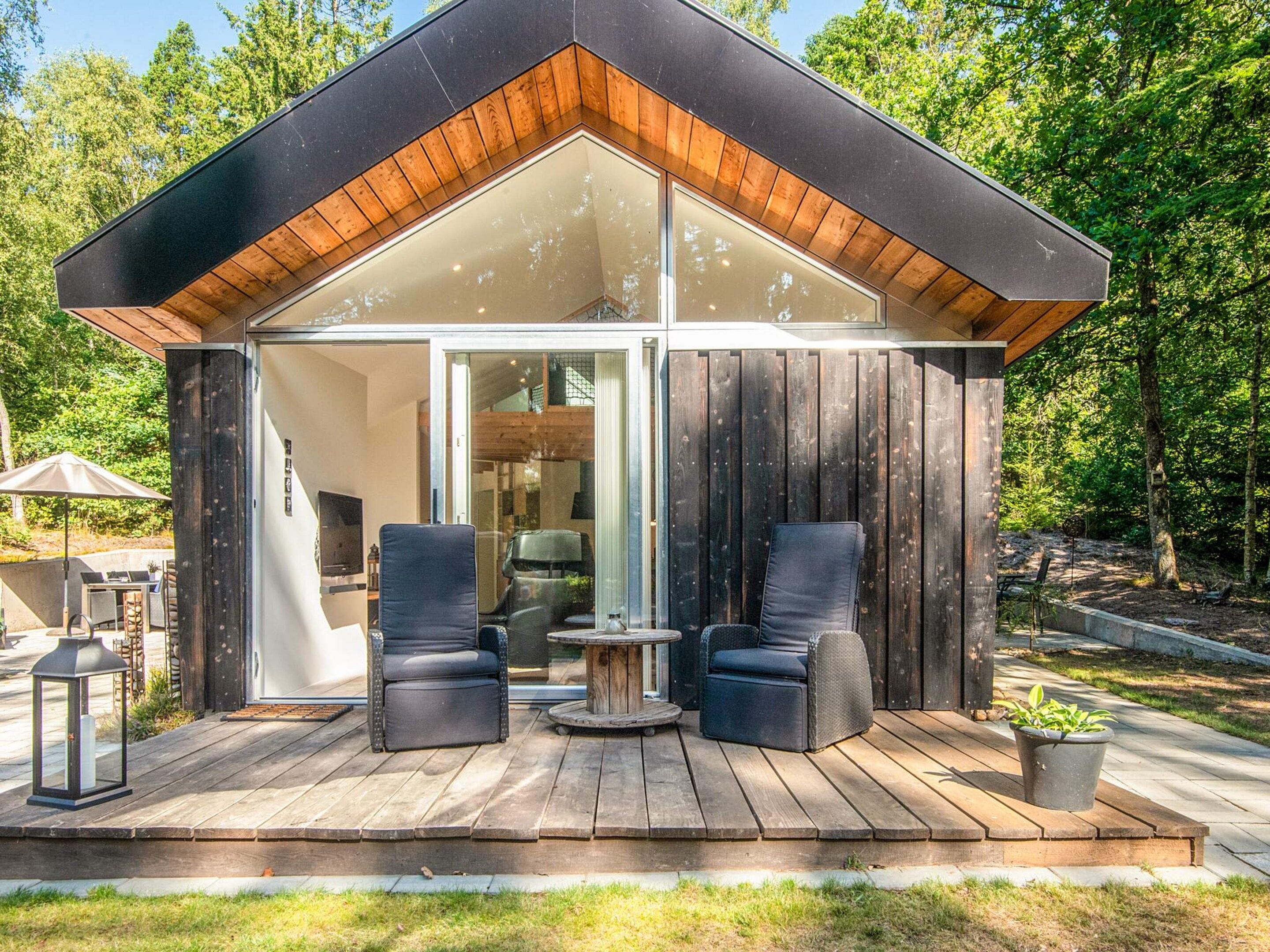 A modern cabin with a deck, two chairs, a table, and a potted plant.