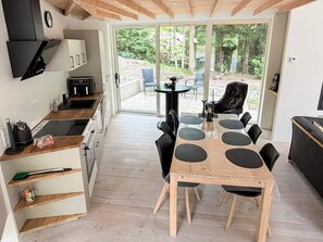 A modern kitchen with a wooden countertop, a dining table with chairs, and a view of a garden through large glass doors. - 5 Star Holiday Home in Ans By (Ans)