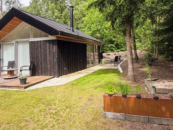 A modern cabin with a deck, a chimney, and a garden area with labeled plants. - 5 Star Holiday Home in Ans By (Ans)