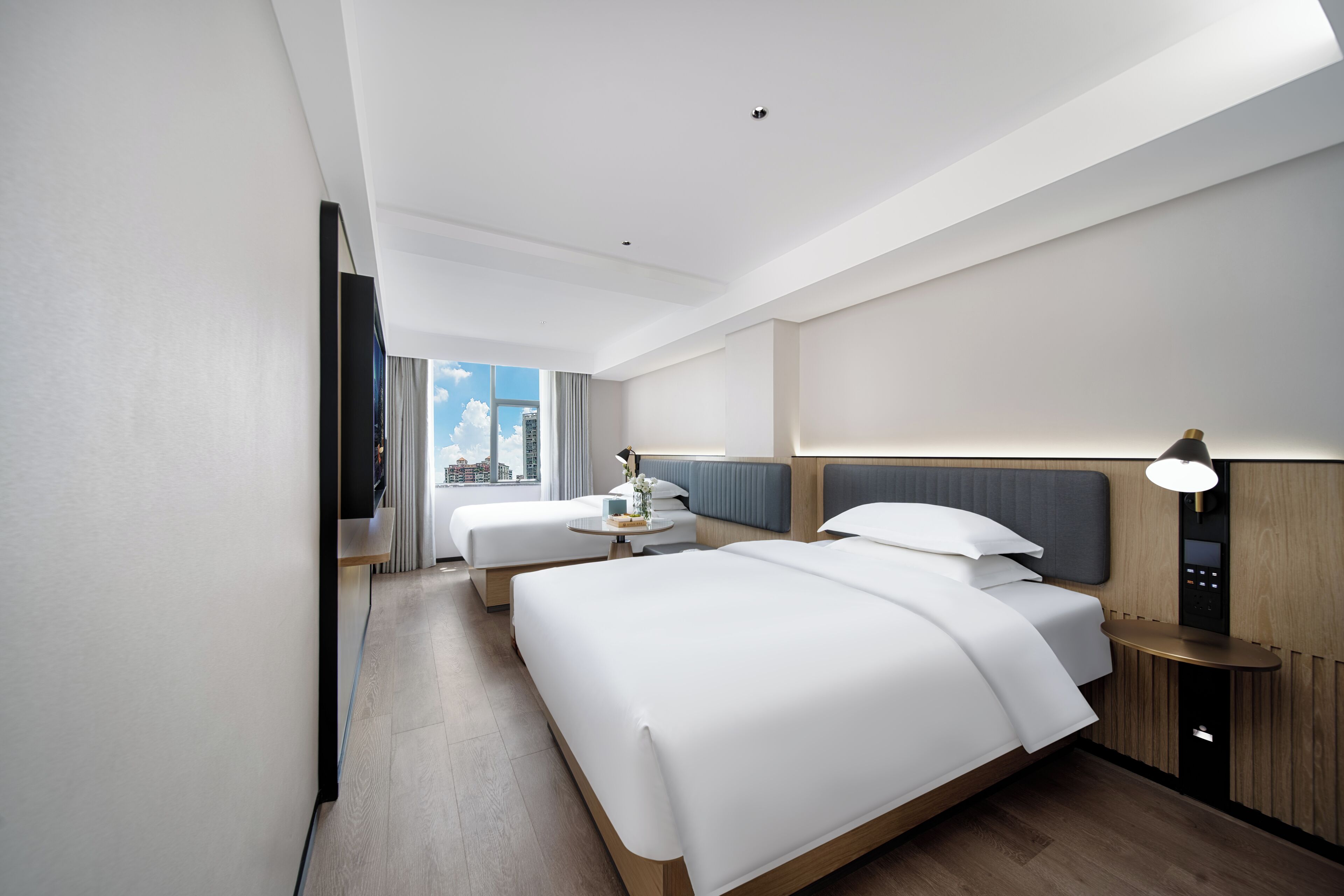 Quarto de hotel moderno com uma cama grande, uma cama menor, uma escrivaninha e uma televisão.