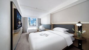 Una habitación de hotel moderna con una cama grande, un escritorio pequeño, un televisor y una ventana con vista a la ciudad.