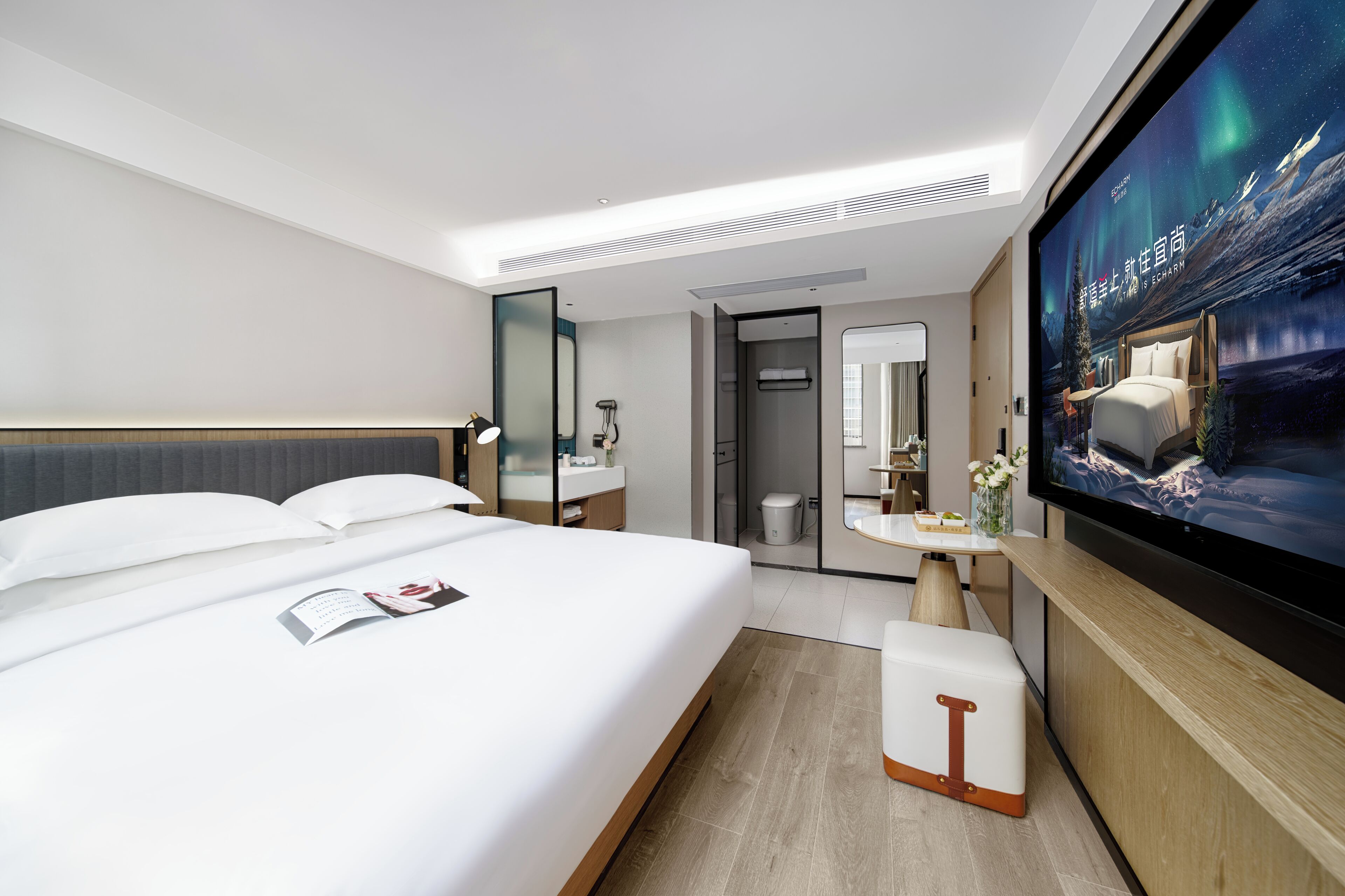 A modern hotel room with a large bed, a TV, a bathroom, and a desk area.