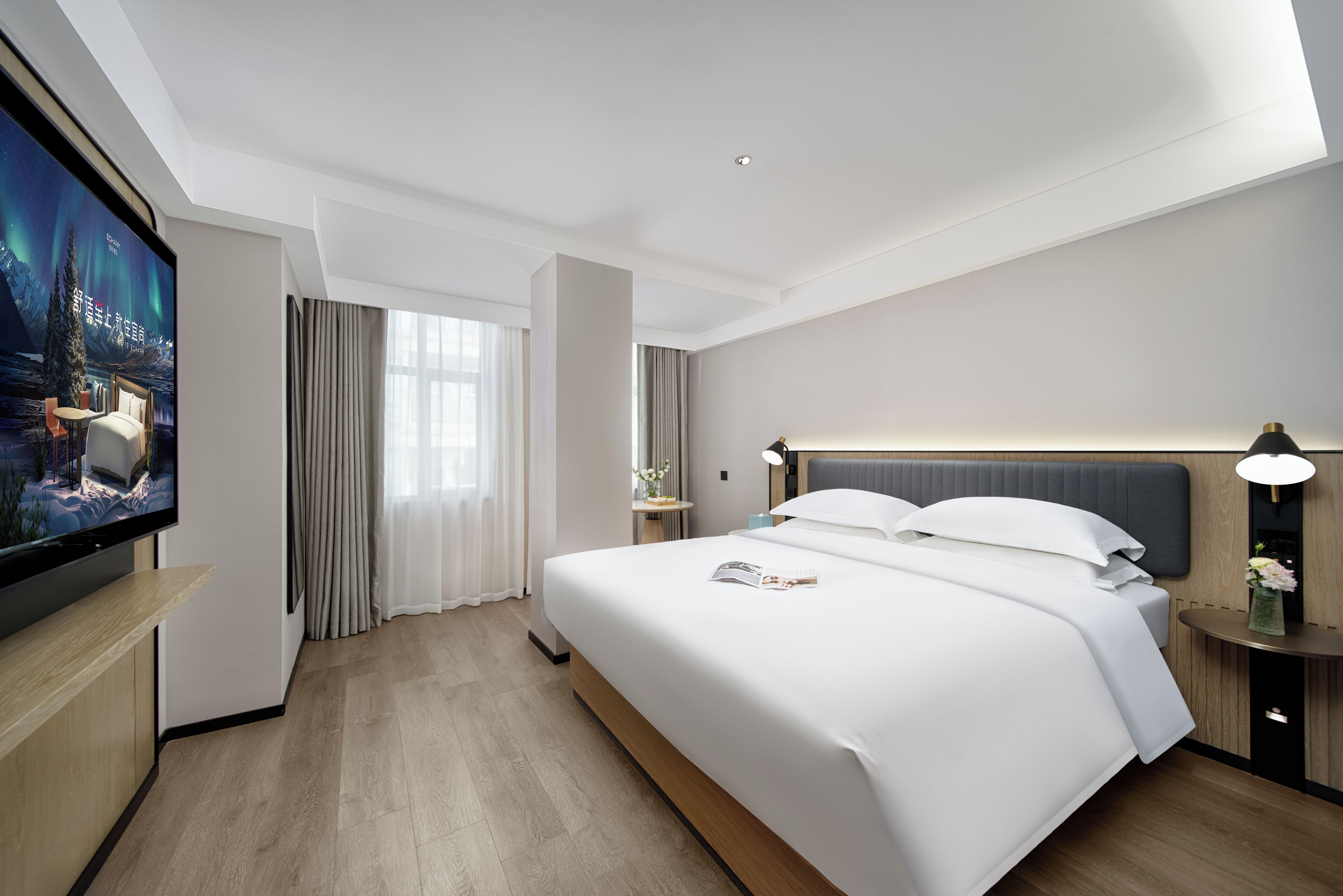 A modern hotel room with a large bed, a flat-screen TV, a bedside table, and a nightstand.