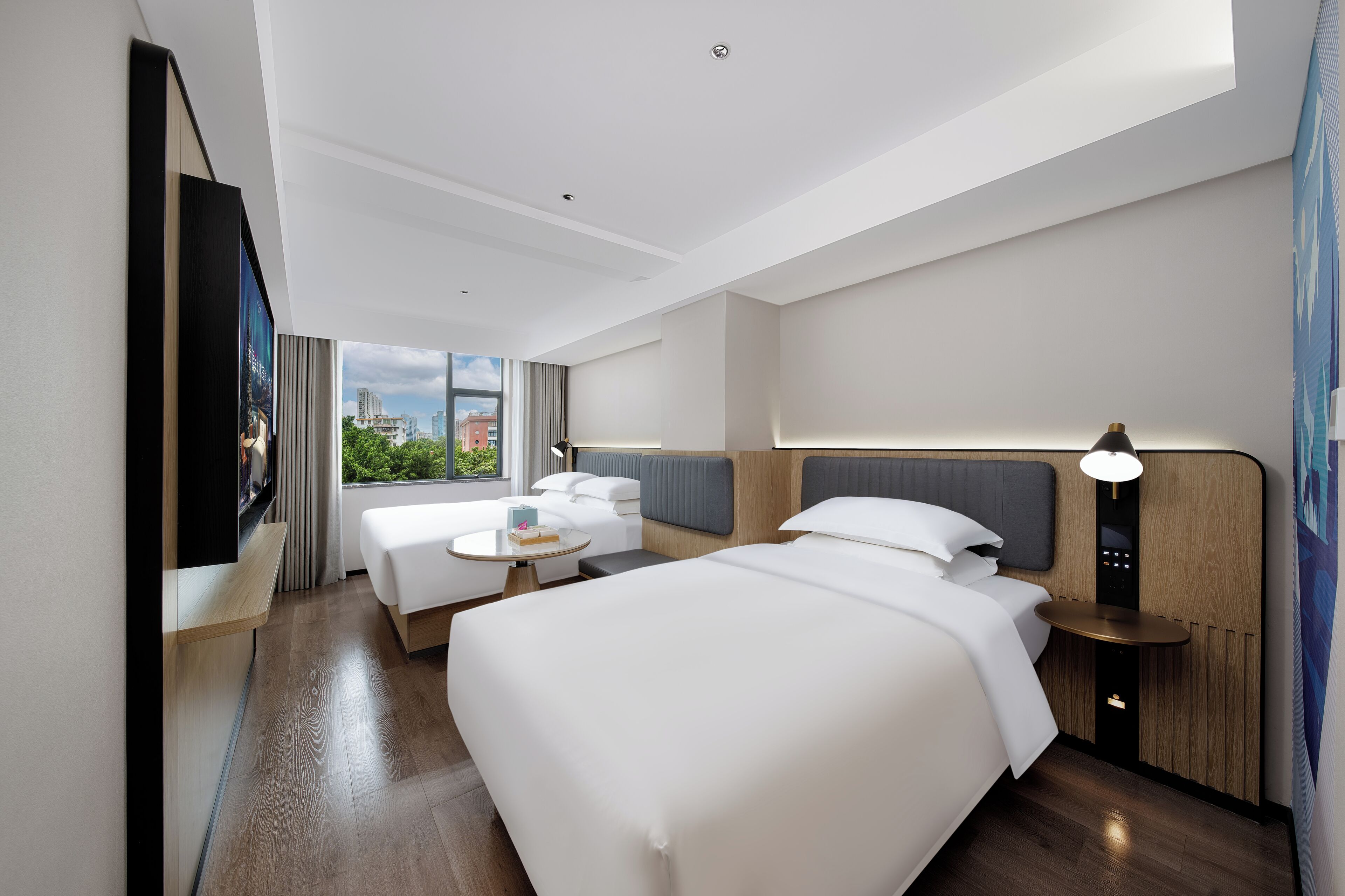 Une chambre d’hôtel moderne, dotée d’un grand lit, d’un petit canapé, d’une table ronde et d’un téléviseur fixé au mur.