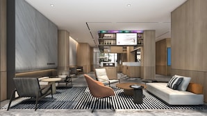Un moderno vestíbulo de hotel con zonas de estar, una recepción y una pantalla de televisión.
