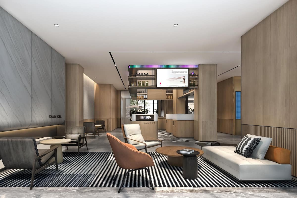 A modern hotel lobby with seating areas, a reception desk, and a TV screen.