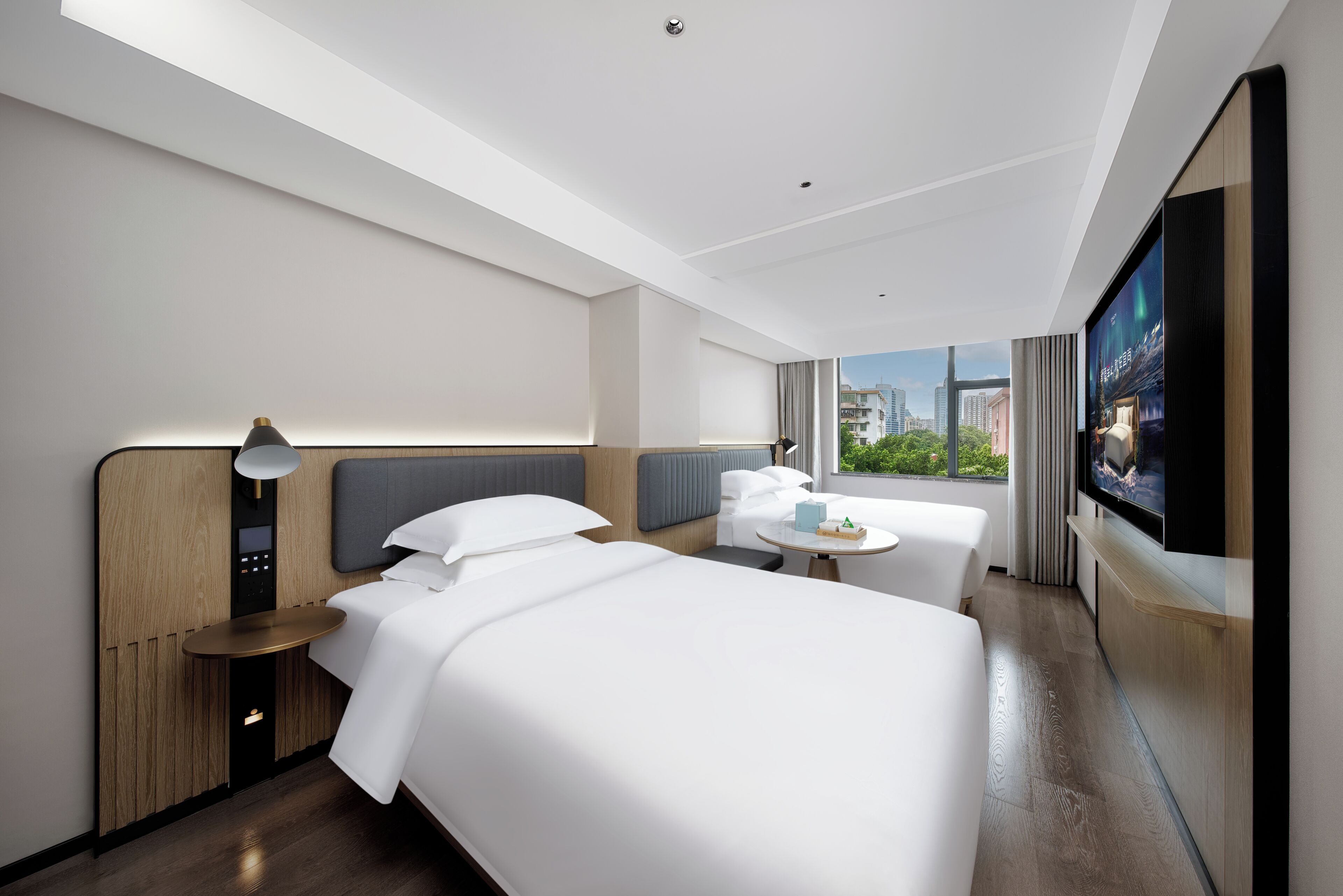 Una camera d'hotel moderna con un letto grande, un letto più piccolo, una scrivania e una televisione.
