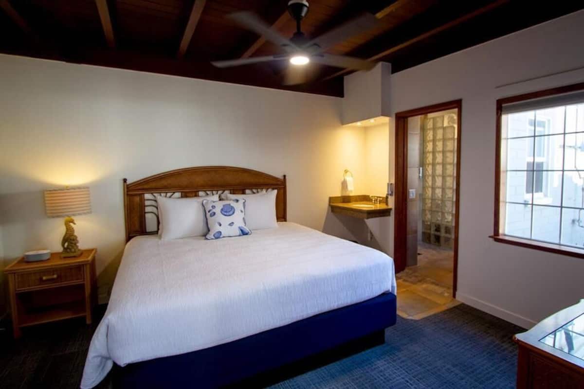 A bedroom with a bed, bedside table, lamp, and a window with a view.