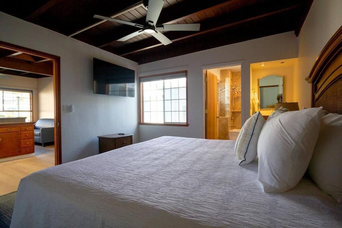 A bedroom with a large bed, a ceiling fan, a window, and a door leading to another room.