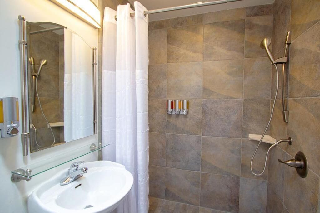 A bathroom with a glass shelf holding toiletries, a white sink, a shower with a glass door, and a wall-mounted mirror.