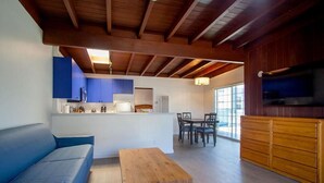Un interior moderno con techo de madera, un sofá azul, una mesa de centro de madera, una zona de cocina y una mesa de comedor con sillas.