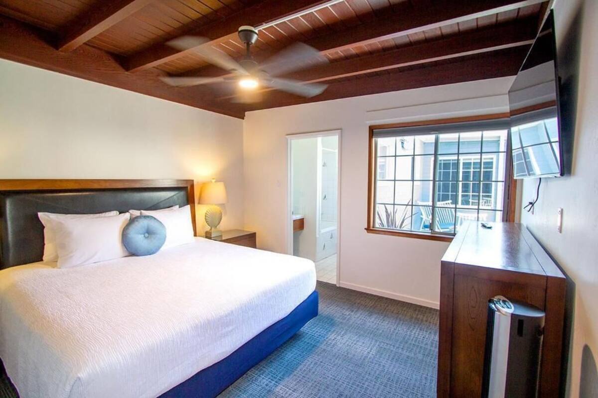 A hotel room with a bed, a ceiling fan, a window with a view, and a desk.