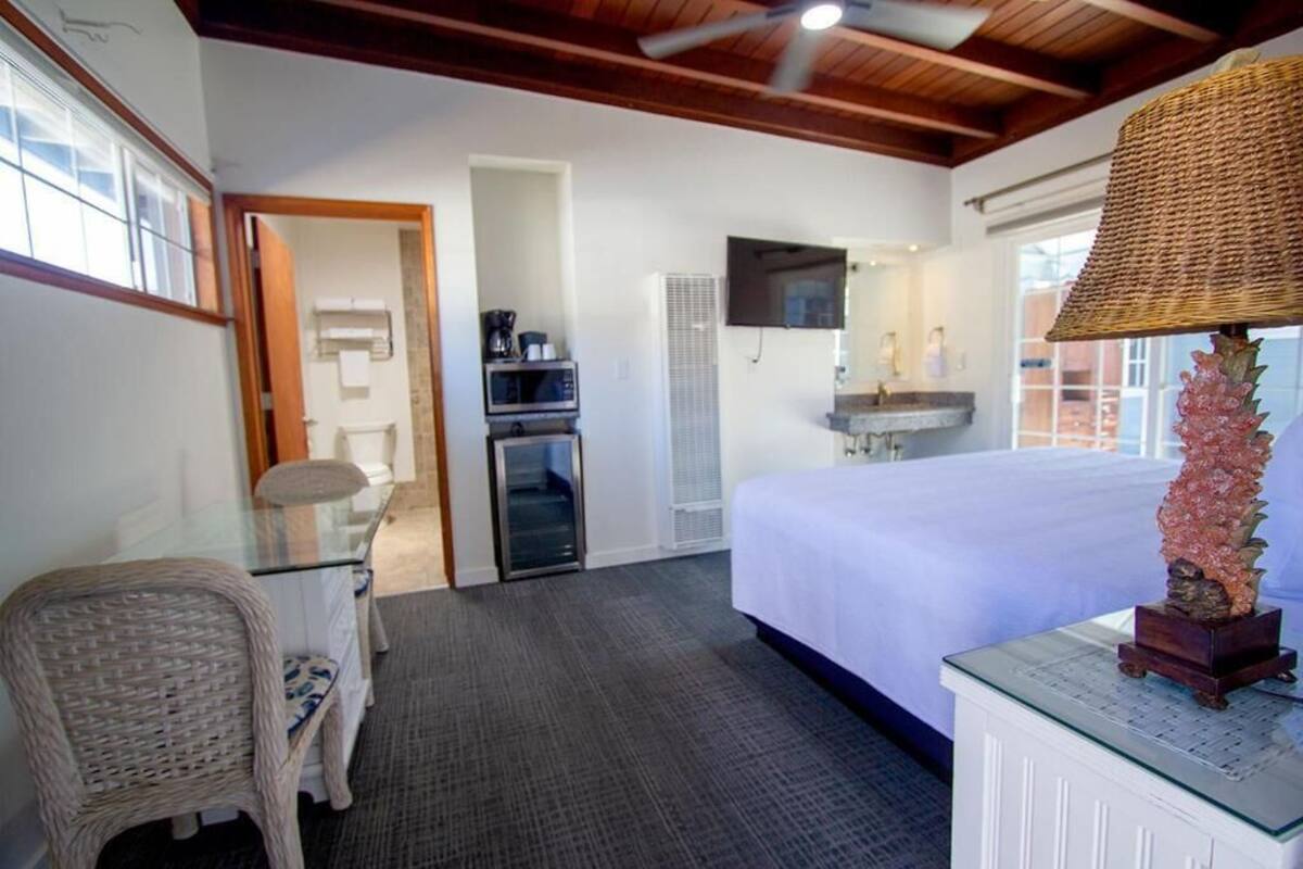 A hotel room with a bed, a television, a desk with a chair, a small refrigerator, and a decorative lamp.
