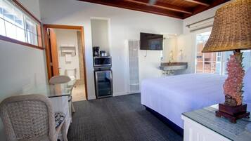 A hotel room with a bed, a television, a desk with a chair, a small refrigerator, and a decorative lamp.
