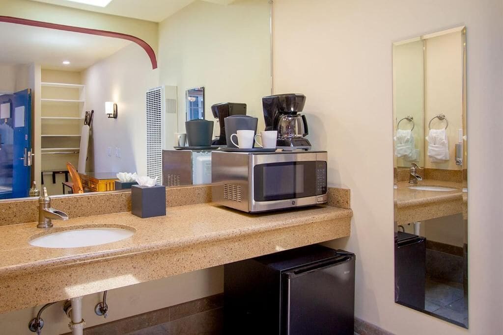 Ein Hotelbad mit Waschbecken, einer Kaffeemaschine, einem Spiegel und einem Mülleimer.