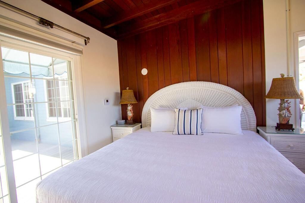 Un dormitorio con una cama grande, paredes de madera, techo blanco y vistas a través de un ventanal.