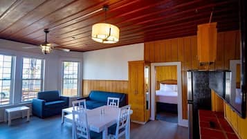 A room with a wooden ceiling, a dining table with chairs, a sofa, and a bed with a wooden door.
