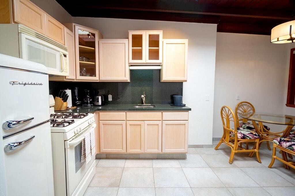 Una cocina con estufa, microondas, armarios y una zona de comedor con sillas.