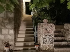 Eine Treppe mit Steinernen Stufen, die nach oben führt, umgeben von Grünpflanzen und Blumentöpfen.