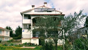 A two-story building with a balcony, surrounded by a garden with various plants and flowers. - Double Room with Balcony (Rovinj)