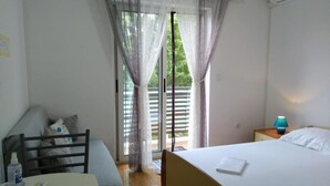 A hotel room with a bed, a table with a remote control, a chair, a nightstand with a lamp, and a window with curtains. - Double Room with Balcony (Rovinj)