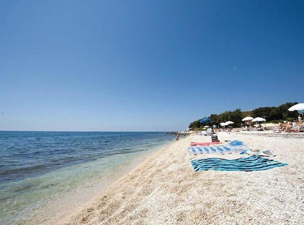 Une plage avec une eau claire, des parasols et des gens.