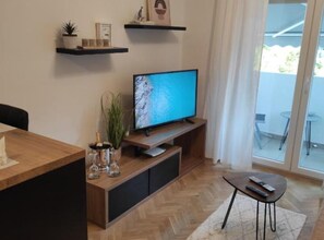Ein modernes Wohnzimmer mit Flachbildfernseher, Holzmöbeln, einer Glastür und Blick durch ein Fenster.